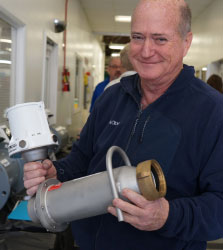 An image of a smiling man holding a silver flow meter with white electronics