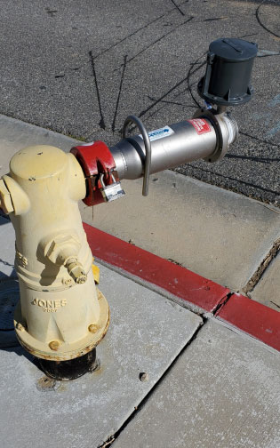 An image of a yellow hydrant, silver meter, black electronics, paved road in the background